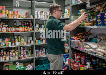 Ein freiwilliger Mann an einem britischen Trussell Vertrauen lokalen Kirche food bank Arbeiten organisiert Spenden auf Regalen Stockfoto