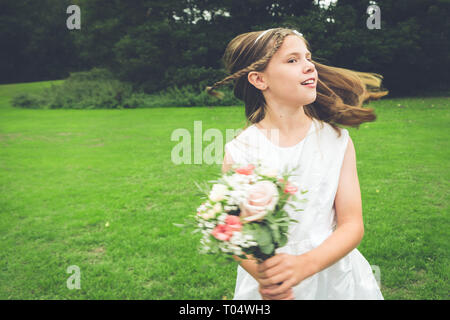 Junge Mädchen Brautjungfer tanzen und Spinnen in einem Park, trug ein weißes Kleid und einem rustikalen Posy Stockfoto