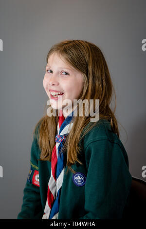 Ein portrait Foto von einem Lachen britischen Mädchen weibliche cub Scout in Uniform mit grünen Sweatshirt, roten, weißen und blauen Halstuch und Schieberegler oder woggle Stockfoto
