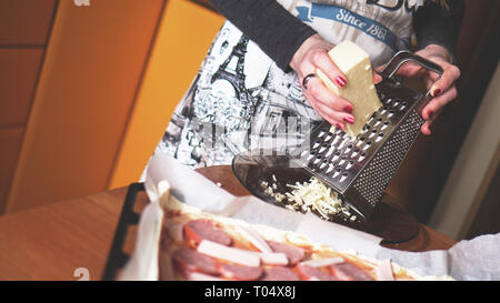 Closeup hand von Chef Baker, hausgemachte Pizza. Weibliche Hände reibt Käse auf der Pizza Stockfoto
