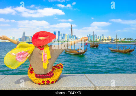 Glückliche Frau an der Küste von Doha Park entlang der Bucht von Doha mit traditionellen Dhau auf Hintergrund. Lifestyle kaukasischen Tourist genießt Osten Mound-Skyline anzeigen Stockfoto