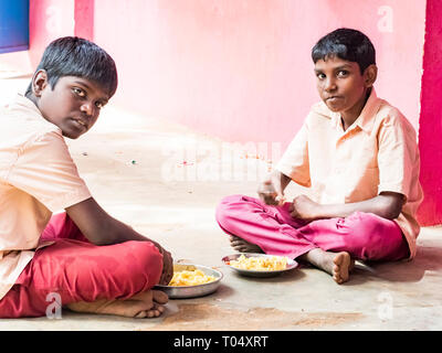 PUDUCHERRY, Tamil Nadu, Indien - Dezember Circa, 2018. Zwei nicht identifizierte armen Mitschüler Jungen mit Uniformen sitzen auf dem Boden im Freien, Essen mit t Stockfoto