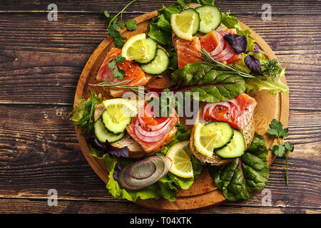 Lachs Sandwich mit grünen, roten Zwiebeln und Gewürze auf einem Holztisch. Stockfoto