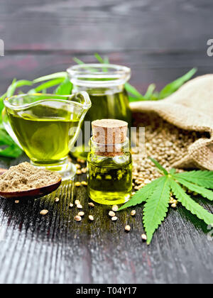 Hanf Öl in zwei Gläsern und sauceboat mit Korn in einen Sack, einen Löffel mit Mehl, Blätter und Stängel von Cannabis auf einem dunklen Holzplatte Hintergrund Stockfoto