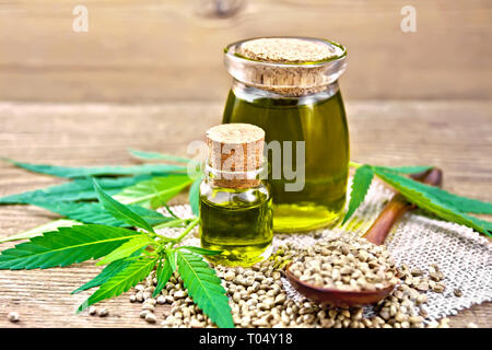Hanf Öl in zwei Gläser, einen Löffel mit Körnern auf eine Serviette von Sackleinen, Blätter und Stängel von Cannabis vor dem Hintergrund einer alten hölzernen Board Stockfoto