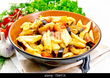 Penne Pasta mit Auberginen und Tomaten in eine Schüssel auf dem Handtuch, Gabel, Knoblauch und Petersilie auf hellem Holz Vorstand Hintergrund Stockfoto