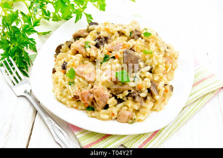 Reis Risotto mit Pilzen, Hähnchen Fleisch, Käse und Knoblauch in eine Platte auf dem Handtuch, Gabel und Petersilie auf dem Hintergrund der hellen Holzmöbeln board Stockfoto