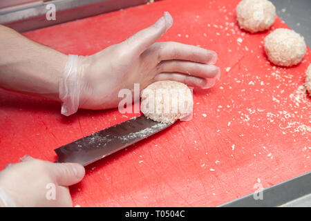 Chef's Hände in Handschuhe anlegen, die Hähnchen Schnitzel mit Messer für Burger. Zutaten. Konzept Restaurant Business, Fast Food, Vorbereitung für c Stockfoto