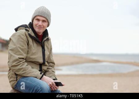 Mann sitzend mit Tablette am Winter Strand Stockfoto