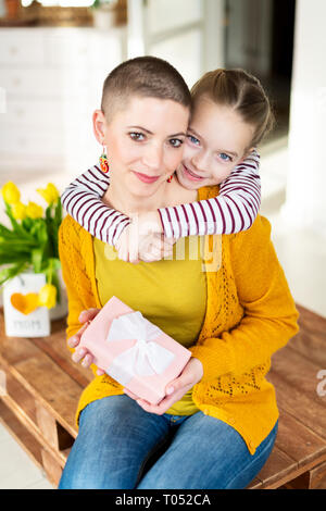 Happy Muttertag oder Geburtstag Hintergrund. Adorable junges Mädchen überraschend ihre Mamma, jungen Krebspatienten, mit Blumenstrauß mit präsentieren. Familienfeier Stockfoto