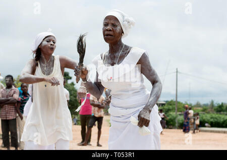 Adzopé, Elfenbeinküste - 31. August 2016: reife Frau in Weiß Halskette mit Pferdeschwanz Hals in der Hand gekleidet Tanzen singen accomgnée durch eine junge Frau in Stockfoto
