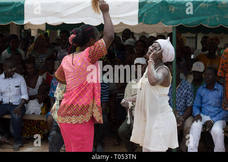 Adzopé, Elfenbeinküste - 31. August 2016: junge Frau in Weiß, Zeichen der Vergebung zu einem anderen vor ihr, gekleidet in Rosa lächelnd, in t Stockfoto