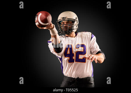 American football player in Uniform mit dem Ball bereitet einen pass zu machen. American football Konzept, schwarzer Hintergrund Stockfoto