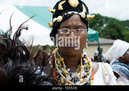 Adzopé, Elfenbeinküste - 31. August 2016: junge frau mit Halsketten, Halskette Tragen einer Brille und Golden Hut stehen und beobachten die Kamera. Stockfoto
