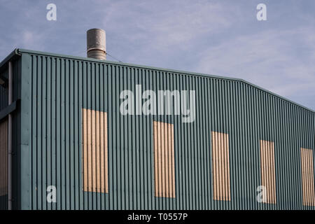 Das Äußere eines grünen und gelben moderner Metal Lager mit einem silbernen Schornstein an einem sonnigen Tag Stapel Stockfoto