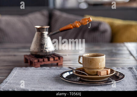 Closeup traditionellen türkischen Kaffee in cezve auf Holz Stativ, Porzellan Tasse mit raffiniertem Zucker Würfel auf dem Tisch im Restaurant serviert. Сoncept frühen Bruch Stockfoto