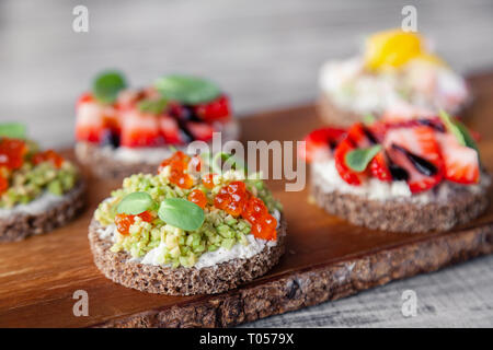 Сloseup Makro Set von verschiedenen nördlichen trendy Aperitifs auf smorrebrod Roggenbrot mit rotem Kaviar und Avocado, Erdbeeren und Balsamico Dressing. Con Stockfoto