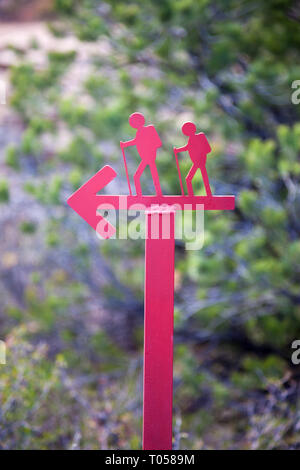 Rote metall Schild mit einer Silhouette von zwei Wanderer auf den Wanderweg zu einem Wanderweg in der Nähe von Blanding, Utah zeigt auf einem unscharfen Hintergrund der Bäume. Stockfoto