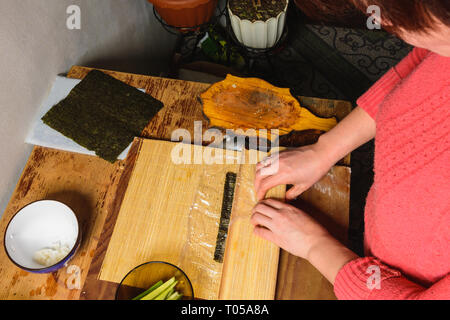 Eine Frau Koch bereitet Sushi in der Küche und wickelt einen Brief an die Nori in der Rolle 2019 Stockfoto