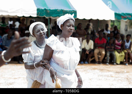 Adzopé, Elfenbeinküste - 31. August 2016: reife Frau in Weiß Halskette Armband mit Pferdeschwanz Arm in der Hand schaut, gekleidet in die Kamera, während ihre Schwester ca Stockfoto