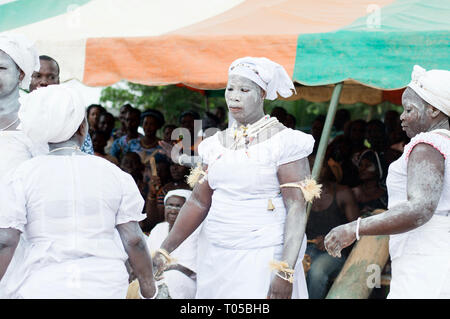 Adzopé, Elfenbeinküste - 31. August 2016: Junge Dame im weißen Pulver auf Ihrem Körper mit Halsbänder und Glocke an ihre zwei Extreme zwei andere gekleidet Stockfoto