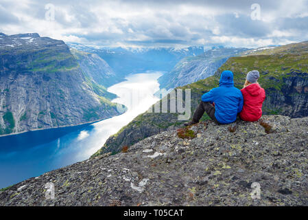 Paar sitzt auf Felsen und blickt auf die Berge in der Nähe von trolltunga. Beliebte Touristenattraktion. Ringedalsvatnet - See in der Gemeinde Odda in Hordalan Stockfoto