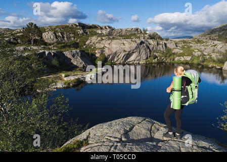 Touristen mit einem Rucksack auf Weg Preikestolen, Norwegen. Blonde Mädchen in einem Mountain Trek. Blauer See auf einem Plateau Stockfoto