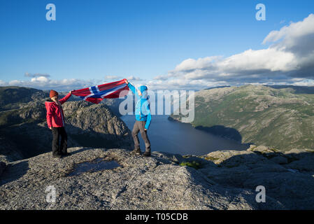 Weg Preikestolen. Paar mit der Flagge von Norwegen. Panorama der Lysefjord. Sonniges Wetter in den Bergen Stockfoto