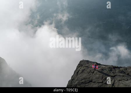 Preikestolen, der berühmte Touristenattraktion in Ryfylke, ragt über den Lysefjord. Mädchen auf einem Felsen mit der Flagge von Norwegen Stockfoto