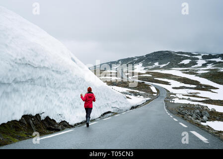 Bjorgavegen - verschneite Straße in Norwegen. Fröhliches Mädchen läuft auf einem Berg Straße in der Nähe einer Wand aus Schnee. Schwere nördlichen Landschaft Stockfoto