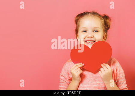 Closeup Portrait von ein süßes kleines Mädchen mit Brötchen der Haare auf einem rosa Hintergrund. Kind mit Herz Stockfoto