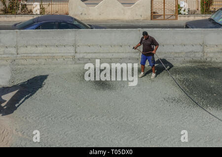 Limassol, Zypern - November 4, 2018: Der Mensch steht in der Mitte des vor kurzem geebnet yard Holding einen Schlauch und sprühen Wasser auf den Kies vor Fl Stockfoto