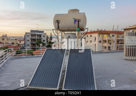 Limassol, Zypern - 4. April 2015: Solarpaneele mit Wassertank auf dem Dach des Gebäudes. An einem sonnigen Abend. Stockfoto