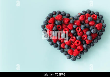 Wald Obst, Himbeeren und Beeren in der Form eines Herzens auf dem blauen Pastellfarben Hintergrund angeordnet, Platz für Text Stockfoto