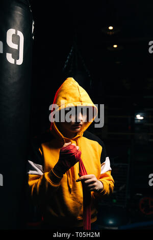 Sportliche Frau Boxer in Gelb sweatshirt zieht rote Bandagen auf ihre Hände. Stockfoto