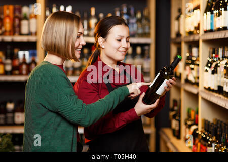 Bild von zwei Frauen mit einer Flasche Wein im Store auf dem Hintergrund der Regale Stockfoto