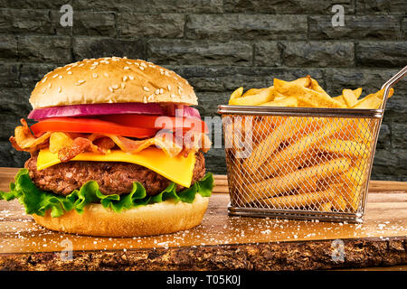 Cheeseburger mit Speck und einen Korb mit Pommes frites. Mauer im Hintergrund. Kopieren Sie Platz für Ihren Text. Stockfoto