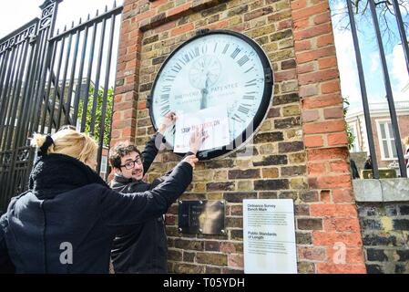 London, Großbritannien. 17 Mär, 2019. Ein Mitglied des Personals hält Aktivist Andreas Pisauro Anhängen einer'S top Die Uhr auf Brexit' Schild Greenwich Wecker neben dem Greenwich Meridian line. Eine britische Druck Gruppe namens "Machen Sie eine Pause vom Brexit und Neue Europäer Irland Protest in Greenwich Park die Heimat von GMT. Eine nationale Kampagne, Gruppe, die gerne Brexit um mindestens ein Jahr verschoben. Credit: Claire Doherty/Alamy leben Nachrichten Stockfoto