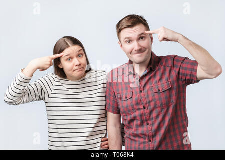 Lustige junge Frau und Mann haben Mimik unzufrieden, Zeigefinger auf Tempel halten, Stockfoto