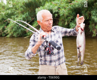 Portrait von zufriedenen Jahren Fischer mit frischen Forellen am Flußufer auf Sommer Stockfoto