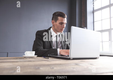 Junge Unternehmer im schwarzen Anzug mit Laptop im Büro Stockfoto