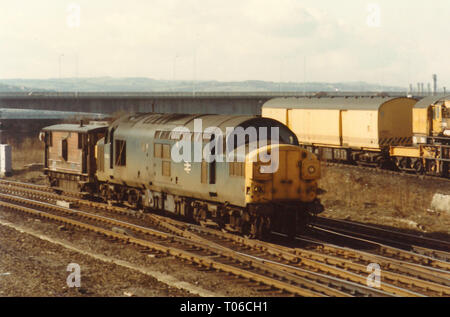 Klasse 37 37088 vorbei Gateshead Depot mit einem wachen van am 5. März 1985 mit einem Zusammenbruch Kran und Redheugh Bridge im Hintergrund. Stockfoto