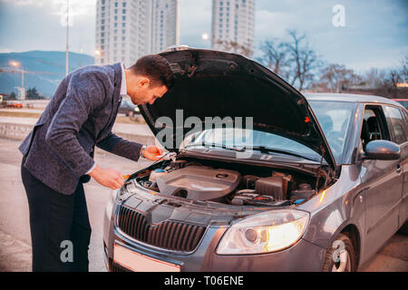 Einen müden Arbeiter steht neben seinem Auto formell gekleidet und Suchen über die Autos Motor Problem besorgt. Stockfoto