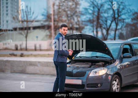 Einen müden Arbeiter steht neben seinem Auto formell gekleidet und Suchen über die Autos Motor Problem besorgt. Stockfoto