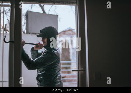 Volle Länge des Hooded mit Brecheisen Glas Tür zu öffnen Mann Stockfoto