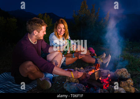 Mann und Frau rosting Würstchen am Lagerfeuer, trinken Bier und ...