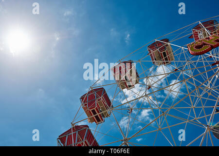 Rote Riesenrad Bild von unten gegen einen blau leuchtenden Himmel mit flauschigen weissen Wolken und Sonne Flare. Stockfoto