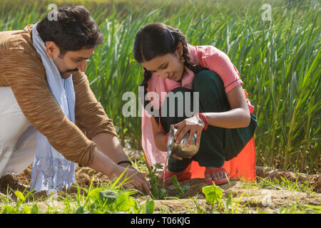 Gerne kleine Mädchen sitzen kleine Pflanzen Bewässerung in der Landwirtschaft Feld zusammen mit ihrem Vater. Stockfoto