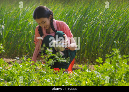 Gerne kleine Mädchen Bewässerung Boden sitzen in der Landwirtschaft. Stockfoto