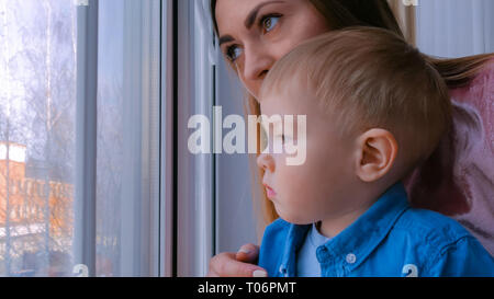 Junge Mutter und nachdenkliche kleine Junge Blick durch Fenster Stockfoto